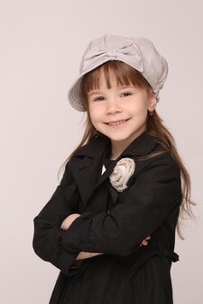 Portrait de petite dame à la mode en manteau noir. fille au chapeau gris joignit les mains.