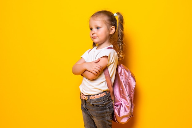 Portrait d'une petite écolière souriante avec sac à dos sur mur jaune
