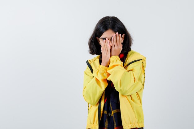 Portrait de petite fille couvrant le visage avec les mains en chemise à carreaux, veste et à la vue de face mélancolique