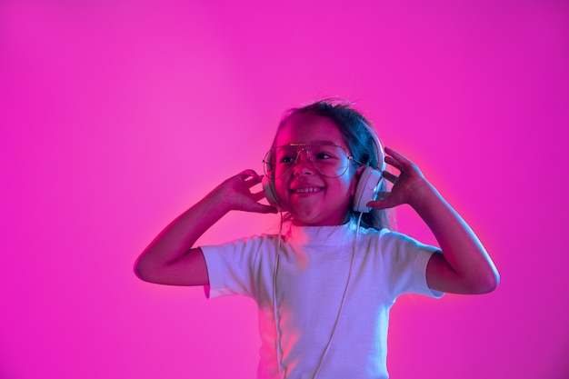 Portrait de petite fille dans les écouteurs sur mur néon violet