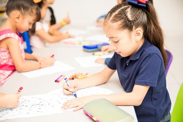 Portrait d'une petite fille faisant une activité de coloriage avec le reste du groupe dans une classe préscolaire