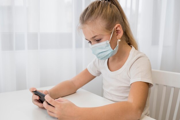 Portrait petite fille avec masque à l'aide de téléphone