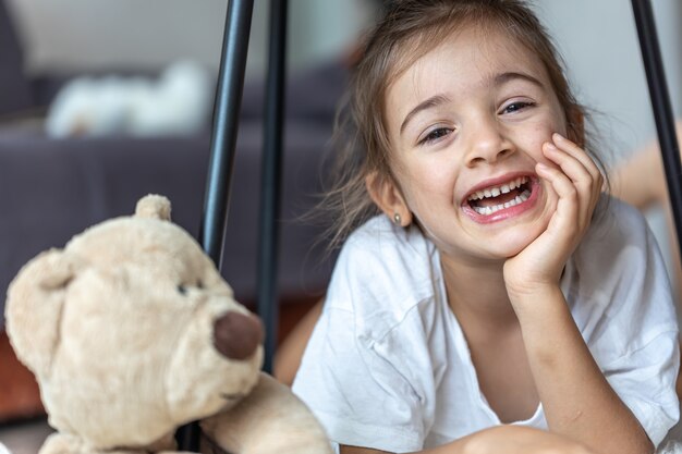 Portrait d'une petite fille qui rit près d'un ours en peluche à la maison.