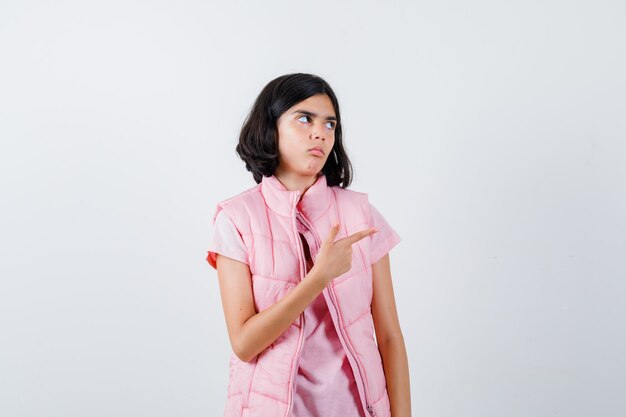 Portrait d'une petite fille en t-shirt blanc et doudoune pointant vers la droite