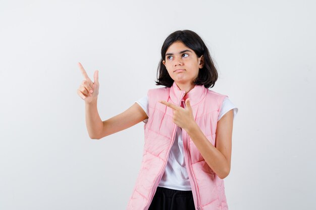 Portrait d'une petite fille en t-shirt blanc et doudoune pointant vers la gauche