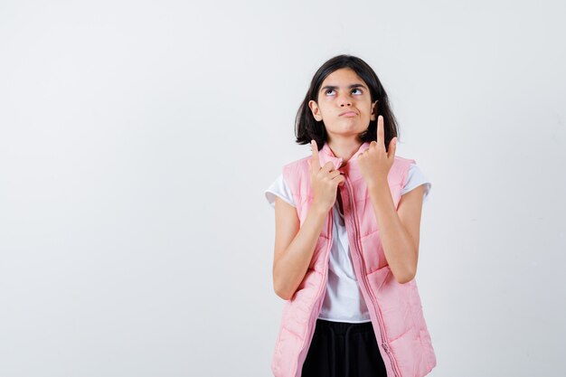 Portrait d'une petite fille en t-shirt blanc et doudoune pointant vers le haut