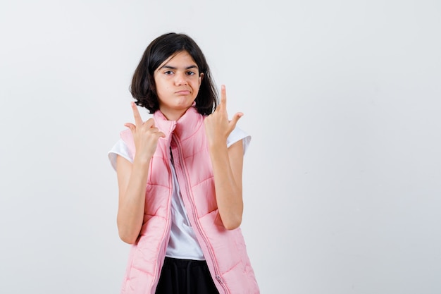 Portrait d'une petite fille en t-shirt blanc et doudoune pointant vers le haut