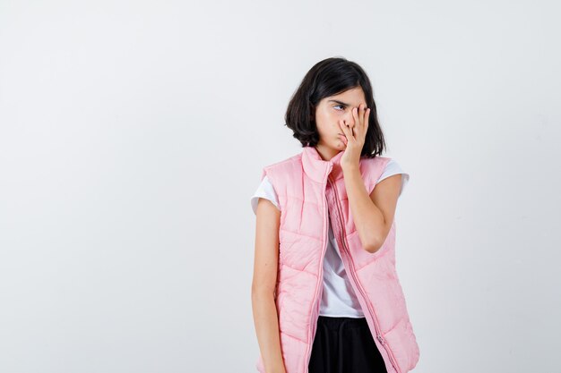 Portrait d'une petite fille en t-shirt blanc et gilet matelassé couvrant le visage