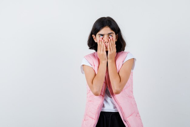 Portrait d'une petite fille en t-shirt blanc et gilet matelassé tirant vers le bas les yeux