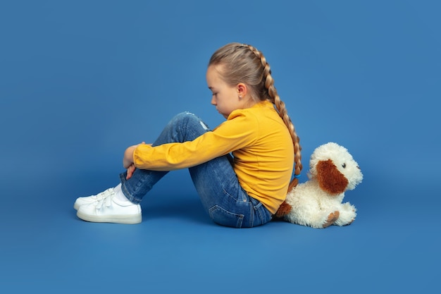 Portrait de petite fille triste assise isolée sur fond bleu.