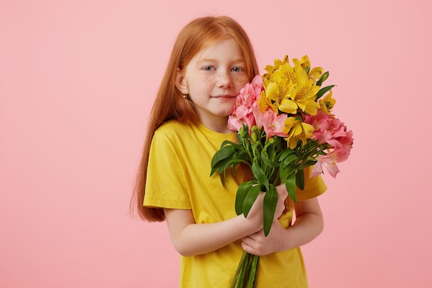 Photo gratuite portrait petite jolie fille rousse de taches de rousseur souriante avec deux queues, tient le bouquet, porte en t-shirt jaune, se dresse sur fond rose.