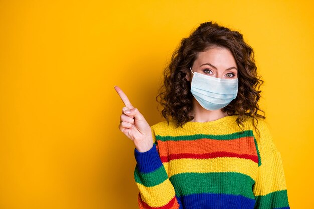 Portrait photo d'une femme pointant un doigt sur un espace vide porter un masque médical isolé sur un fond de couleur jaune vif