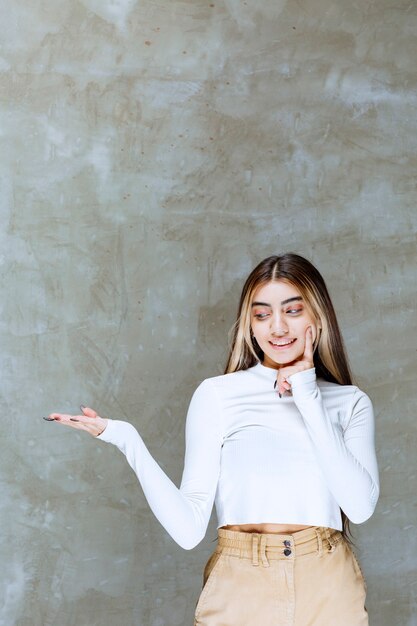 Portrait photo d'un modèle de fille souriante debout et montrant la paume ouverte