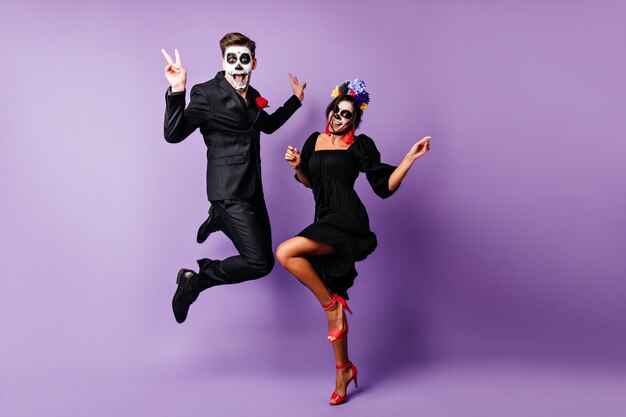 Portrait en pied d'un couple européen dansant sur fond violet en costumes de zombies. Des jeunes drôles s'amusant à l'événement d'halloween.
