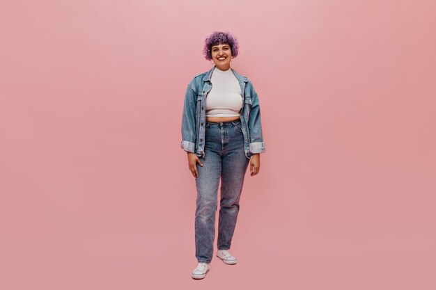 Photo gratuite portrait en pied de femme joyeuse aux cheveux violets courts en costume en jean, baskets blanches et haut léger souriant