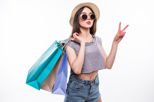 Portrait en pied d'une fille heureuse excitée dans des vêtements colorés lumineux tenant des sacs tout en se tenant debout et montrant le geste de paix isolé