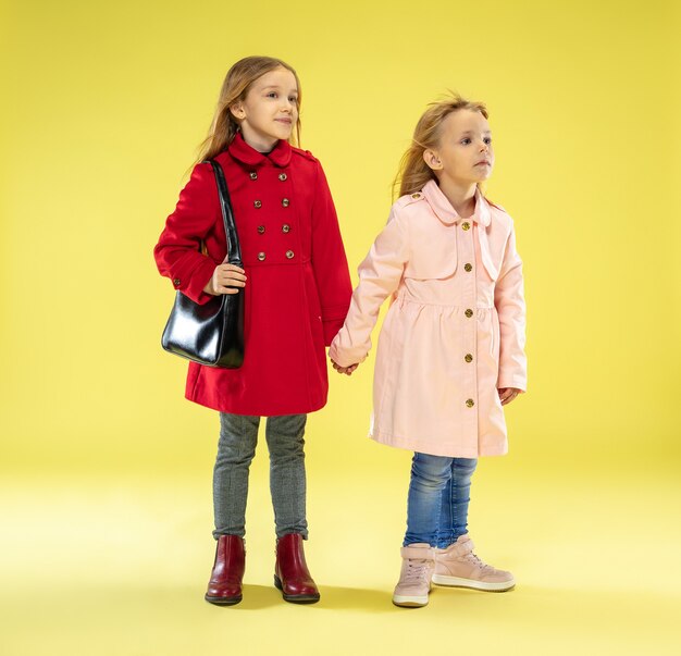 Un portrait en pied d'une fille à la mode lumineuse dans un imperméable tenant un sac noir sur le mur jaune du studio