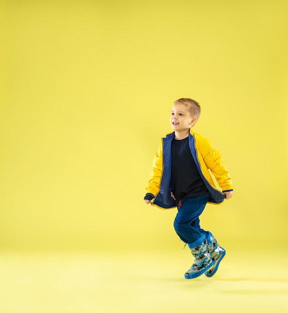 Un portrait en pied d'un garçon à la mode lumineux dans un imperméable courir et s'amuser sur le jaune.