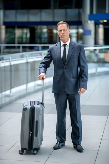 Portrait en pied d'un homme caucasien élégant d'âge moyen sérieux avec la valise debout à l'aéroport