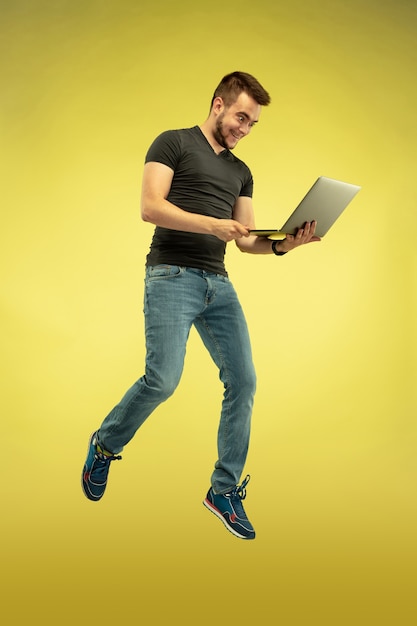 Portrait en pied de l'homme sautant heureux avec des gadgets isolés sur jaune