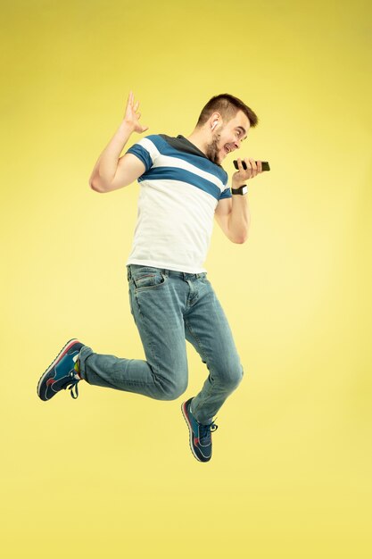 Portrait en pied de l'homme sautant heureux avec des gadgets sur jaune