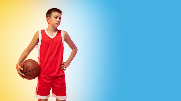 Portrait en pied d'un jeune basketteur avec ballon sur fond dégradé