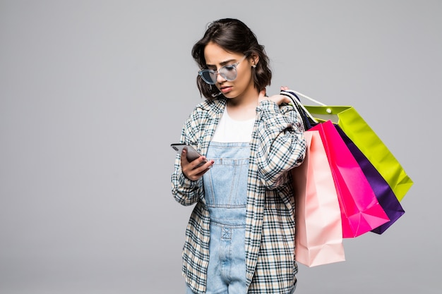 Portrait en pied d'une jeune femme heureuse tenant des sacs à provisions et un téléphone mobile isolé