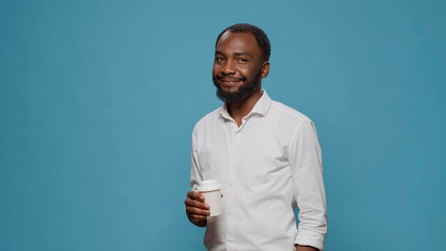 Portrait d'un pigiste masculin appréciant une tasse de café en studio, tenant une tasse avec une boisson au lait pendant la pause de travail et le délai d'attente. Directeur exécutif souriant et buvant un expresso au petit déjeuner.