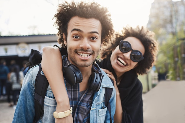 Photo gratuite portrait en plein air d'un couple afro-américain étreignant et souriant largement à la caméra tout en marchant dans le parc et en exprimant des émotions positives.