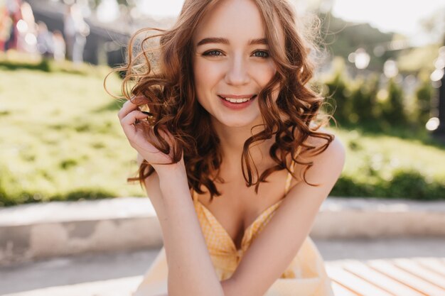 Portrait en plein air d'élégante fille au gingembre touchant ses boucles sur la nature. Incroyable dame européenne aux cheveux rouges posant dans le parc.