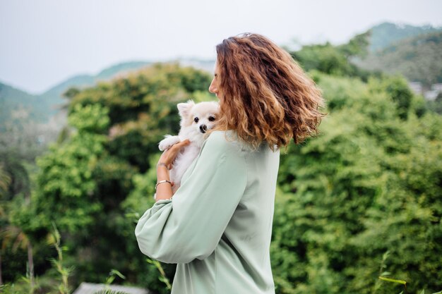 Portrait en plein air de femme bronzée européenne bouclés détient happy pet dog pomeranian spitz