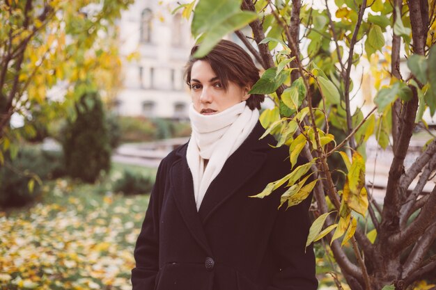 Portrait en plein air de femme dans le parc portant manteau noir d'hiver et écharpe blanche