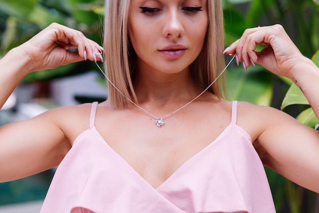 Portrait en plein air de femme en robe romantique rose portant un collier