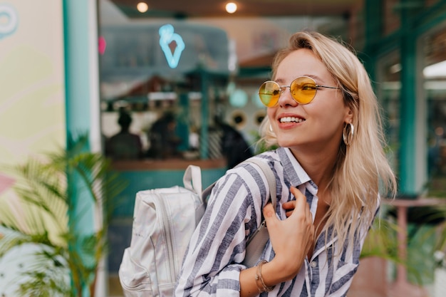 Photo gratuite portrait en plein air de jolie femme blonde portant des lunettes orange avec sac à dos