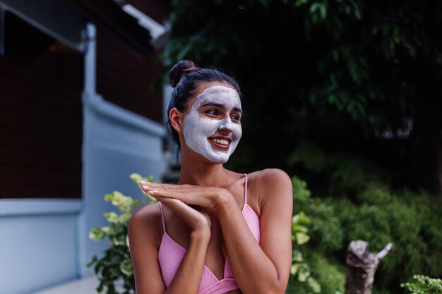 Portrait en plein air de la peau bronzée calme jolie femme caucasienne en bikini au spa avec masque peeling blanc sur le visage