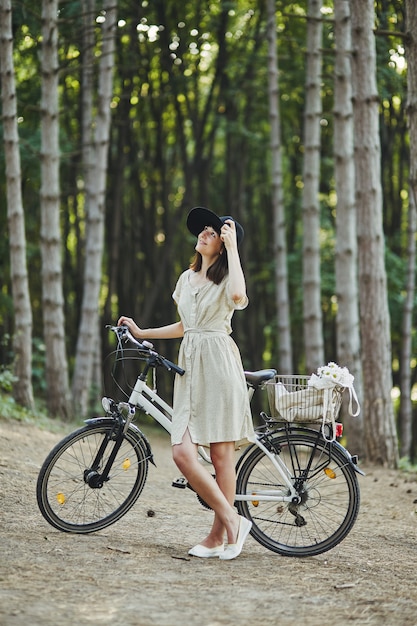 Portrait en plein air de séduisante jeune brune au chapeau sur un vélo.