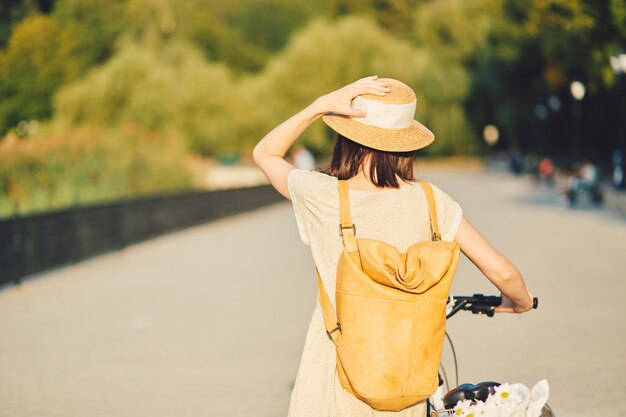 Portrait en plein air de séduisante jeune brune au chapeau sur un vélo.