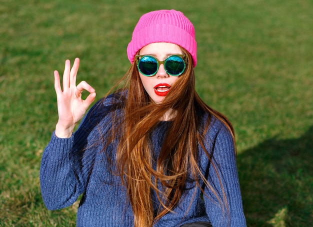 Portrait positif ensoleillé de femme hipster souriante heureuse, posant au parc, voyage, vacances, joie, montre v par ses trouveurs, humeur de printemps, pull et chapeau.