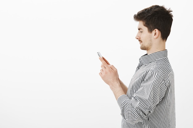 Portrait de profil de petit ami caucasien heureux insouciant avec moustache et barbe, tenant le smartphone, regardant l'écran focalisé, taper un message à un ami