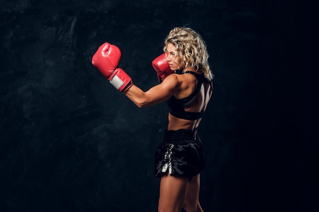 Photo gratuite portrait d'une puissante boxeuse forte en gants rouges sur fond sombre.