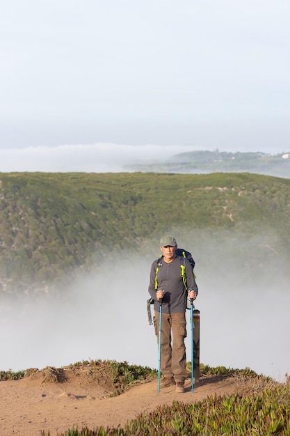 Portrait d'un randonneur heureux aux cheveux gris. Homme en vêtements décontractés avec munitions de randonnée regardant la caméra, paysage spectaculaire en arrière-plan. Passe-temps, concept nature