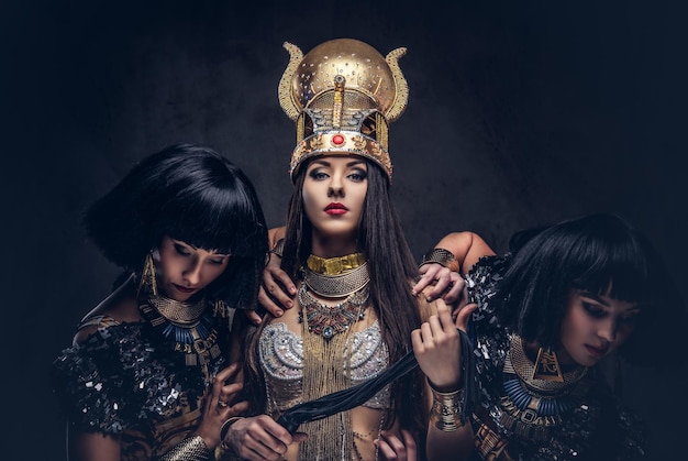 Portrait d'une reine égyptienne hautaine dans un ancien costume de pharaon avec deux concubines. Isolé sur un fond sombre.