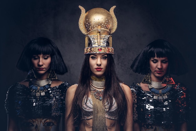 Photo gratuite portrait d'une reine égyptienne hautaine dans un ancien costume de pharaon avec deux concubines. isolé sur un fond sombre.