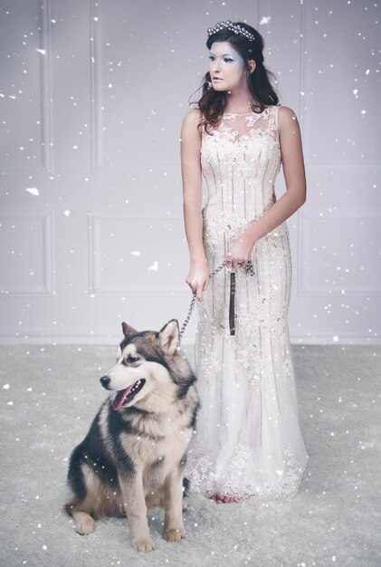 Portrait de la reine des glaces et chien de traîneau parmi la neige qui tombe