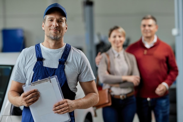 Portrait d'un réparateur automobile heureux regardant la caméra pendant que ses clients se tiennent en arrière-plan