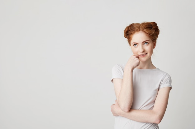 Portrait de rêveuse jeune jolie fille aux cheveux rouges pensant rêver toucher le menton.