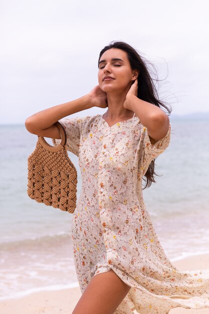 Portrait romantique de femme en robe longue sur la plage au jour nuageux venteux.