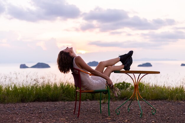 Portrait romantique de jeune femme caucasienne en robe d'été profitant de la détente dans le parc sur la montagne avec une vue imprenable sur la mer tropicale