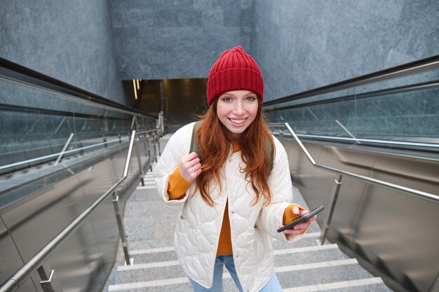 Portrait rousse touriste monte les escaliers avec le smartphone suit l'itinéraire sur l'application de téléphone mobile détient