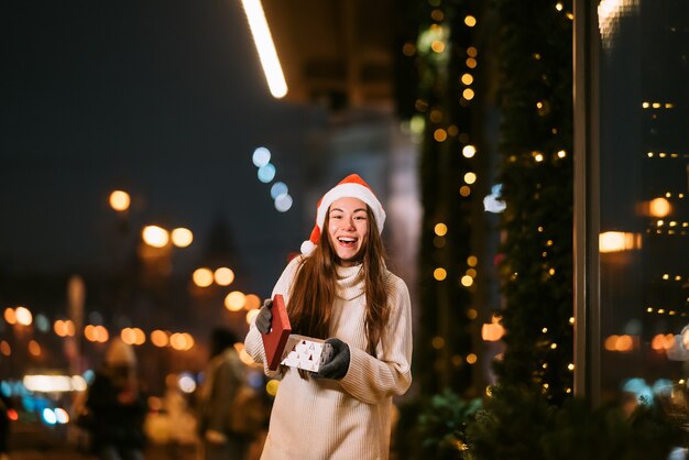 Portrait de rue de nuit de la belle jeune femme agissant ravi. Lumières de guirlande festives.